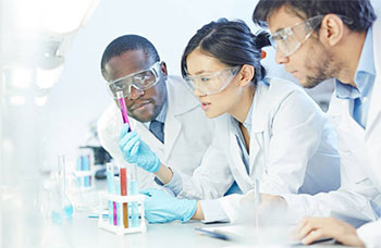 Three young researchers in labcoats looking at a test tube