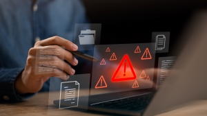 Person using a laptop with a digital warning icon and alert symbols displayed on the screen, representing reporting or compliance issues.