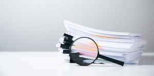 A stack of documents with a magnifying glass on top, symbolizing inspection or detailed review.